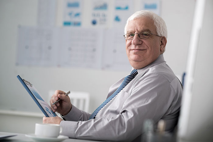 A smiling man in a shirt and tie holding a clipboard, perhaps revealing industry secrets about why fewer people would fly.