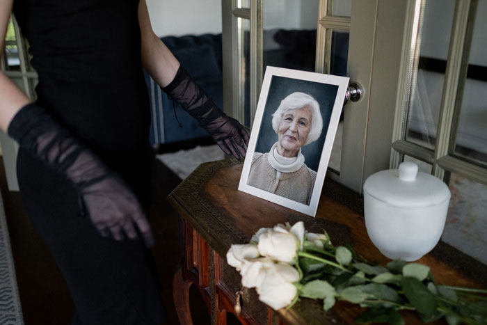 Woman in black at a funeral, beside a photo of grandma, with flowers and an urn. Woman in black at a funeral, beside a photo of grandma, with flowers and an urn.