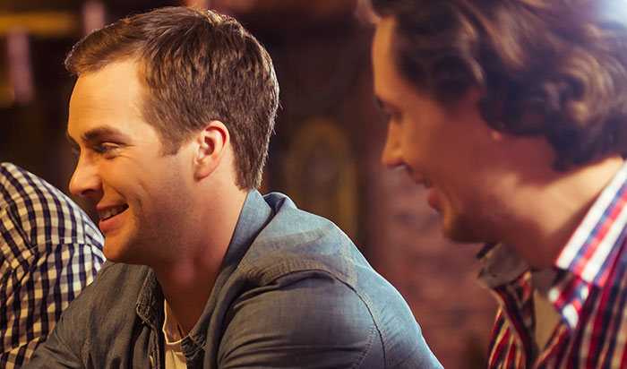Two men smiling and talking, likely at a bar crawl, one wearing a denim shirt, the other a plaid shirt. Two men smiling and talking, likely at a bar crawl, one wearing a denim shirt, the other a plaid shirt.