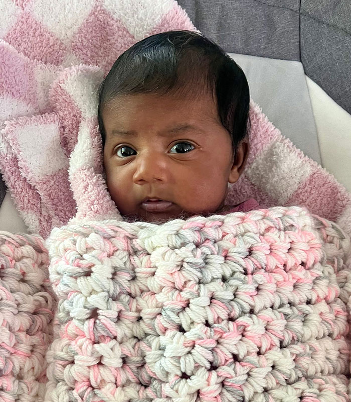 Close-up of a baby's face, wrapped in pink and white blankets, after an IVF mix-up and baby revealed.