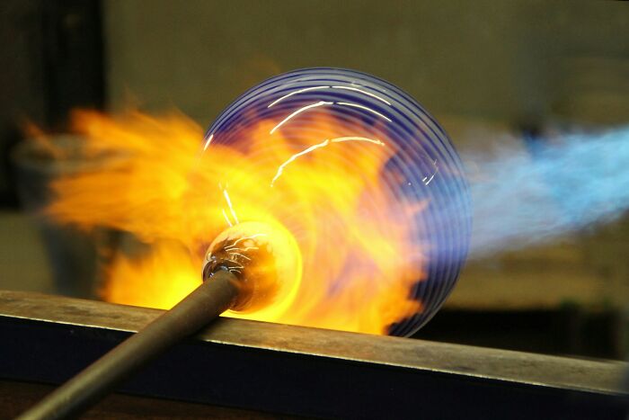 A glassblower working on a spherical piece of glass with flames, an unusual job that people managed to get hired for.