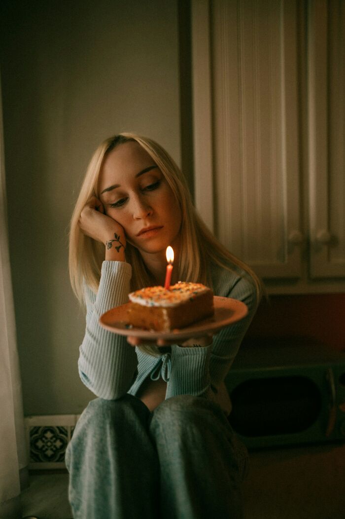 A divorced woman sitting alone, looking sad while holding a slice of cake with a lit candle, representing the moment her marriage was over.