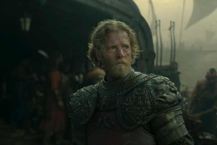 A bearded man in ornate armor stands on a ship deck, ready for a brutal naval clash in House of the Dragon. A bearded man in ornate armor stands on a ship deck, ready for a brutal naval clash in House of the Dragon.