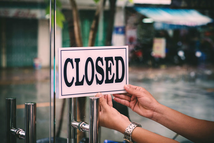Hands putting up a 'CLOSED' sign, symbolizing a company taken down by an employee seeking revenge for being fired.