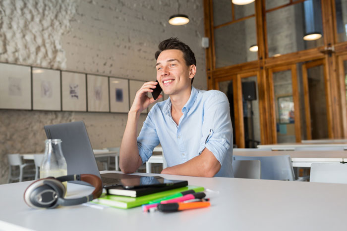 Smiling man on phone at table with laptop and colorful markers, related to being unjustly fired for stealing.