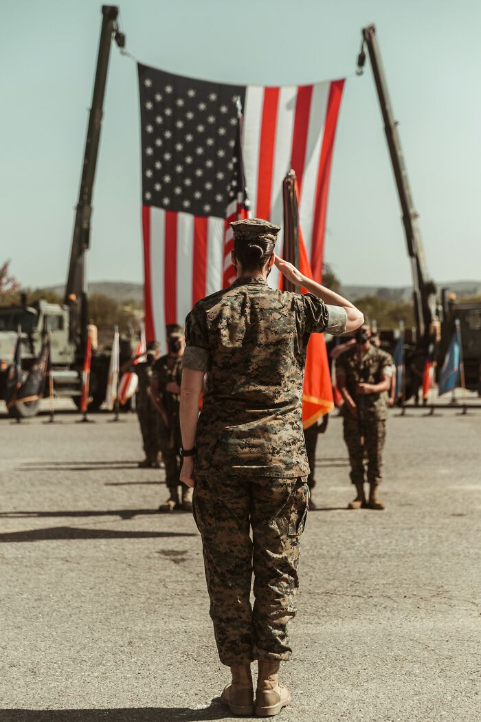 Military personnel saluting in front of large American flags outdoors
