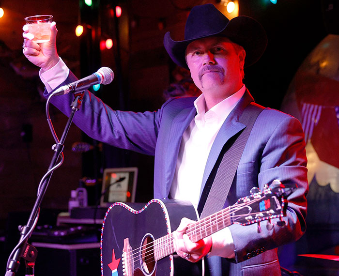 Musician in cowboy hat with guitar raising a glass at a Freedom 250 concert event