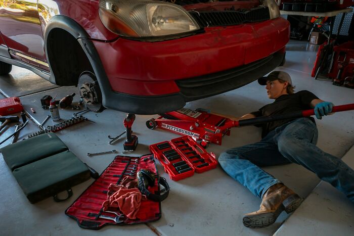 A person repairing a car, using a jack and tools. This shows a moment of self-reliance for divorced people.