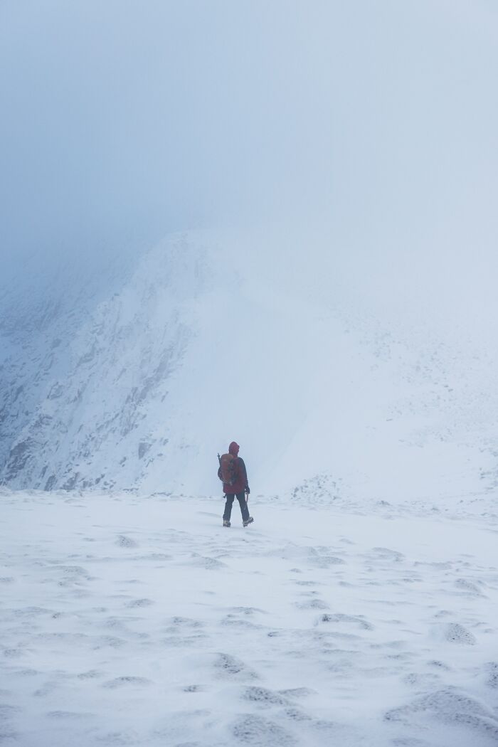 A lone hiker with a red jacket and backpack walks across a vast, snow-covered landscape shrouded in fog, symbolizing unsolved mysteries.