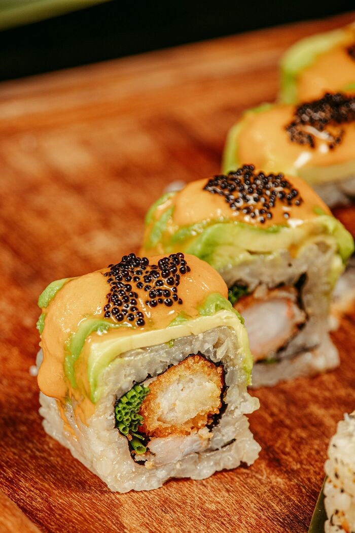 Close up of sushi rolls with sauce and fish roe topping on wooden surface