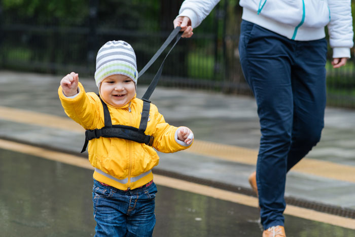 Smiling child wearing a safety harness held by parent walking outdoors