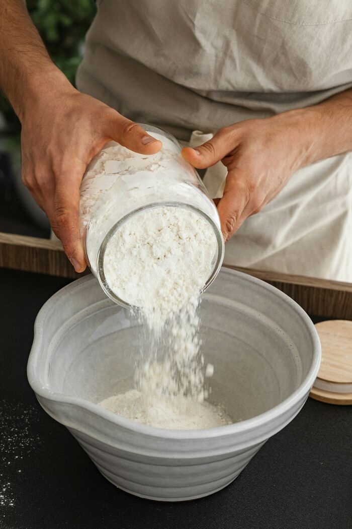 Hands pouring flour into a mixing bowl for baking