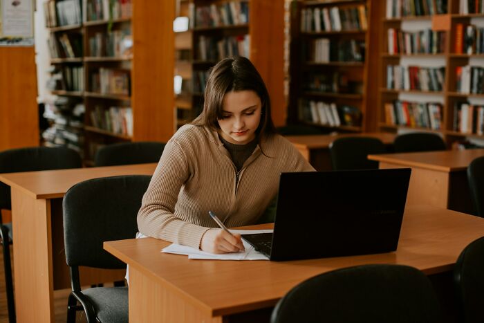 Girl studying with laptop in library for Gen Alpha illiteracy improvement