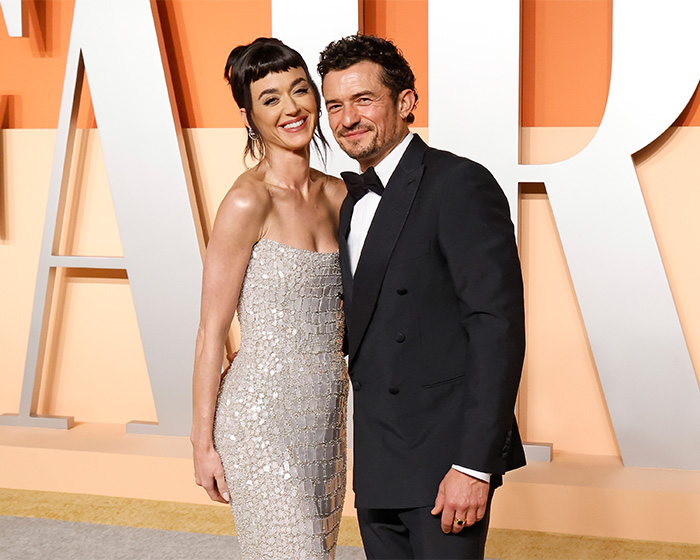 Katy Perry and Orlando Bloom smiling together at an event, with Katy wearing a sparkly dress.