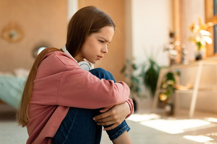 A sad and lonely daughter feeling replaced by her stepkids, sitting on the floor. A sad and lonely daughter feeling replaced by her stepkids, sitting on the floor.