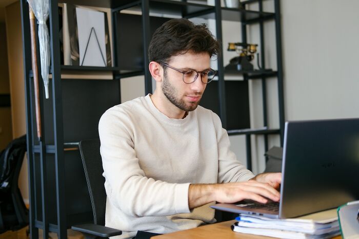 A man with glasses working on a laptop at a desk, showcasing one of many unusual jobs.