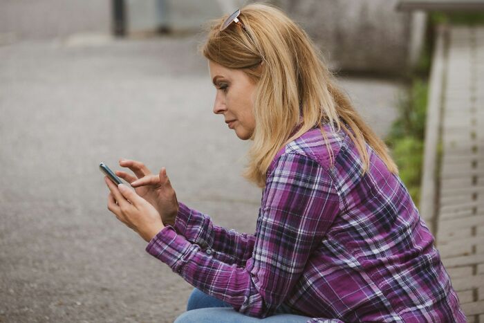 Woman in purple plaid shirt looking shocked at phone screen outside