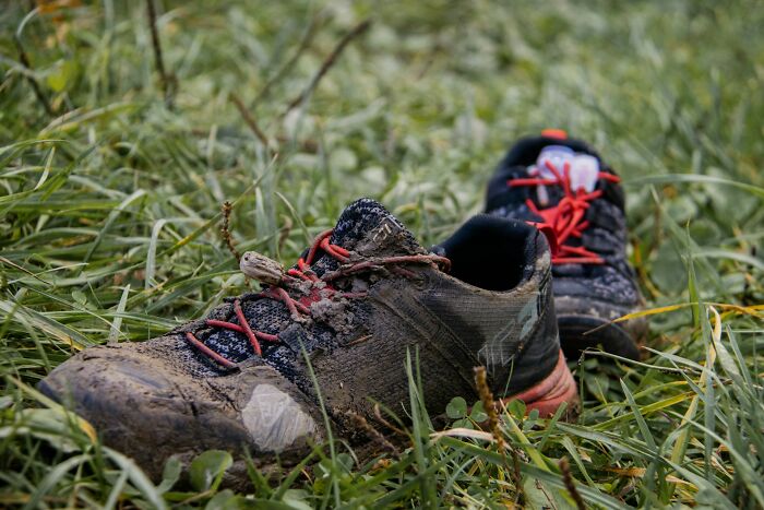 Mud-covered running shoes lying in green grass, an unusual state for footwear after an outdoor activity.