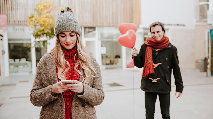 A man holding heart-shaped balloons approaches a woman looking at her phone, depicting a restaurant emergency room situation.