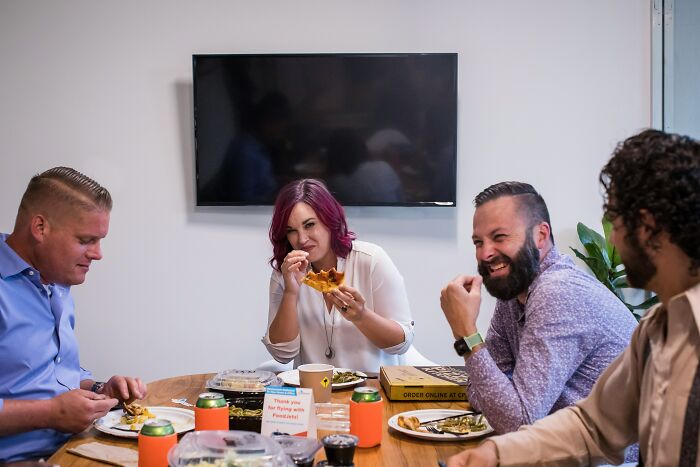 Four people having pizza at a table, laughing and talking, after someone hilariously misread social cues.