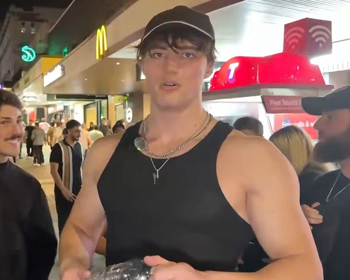 Looksmaxxer Androgenic in a black tank top and cap on a city street, reflecting on his interaction. Looksmaxxer Androgenic in a black tank top and cap on a city street, reflecting on his interaction.