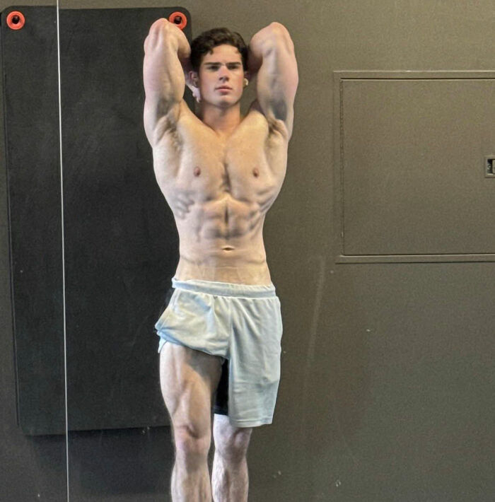Muscular young man posing shirtless in gym wearing shorts showing defined abs