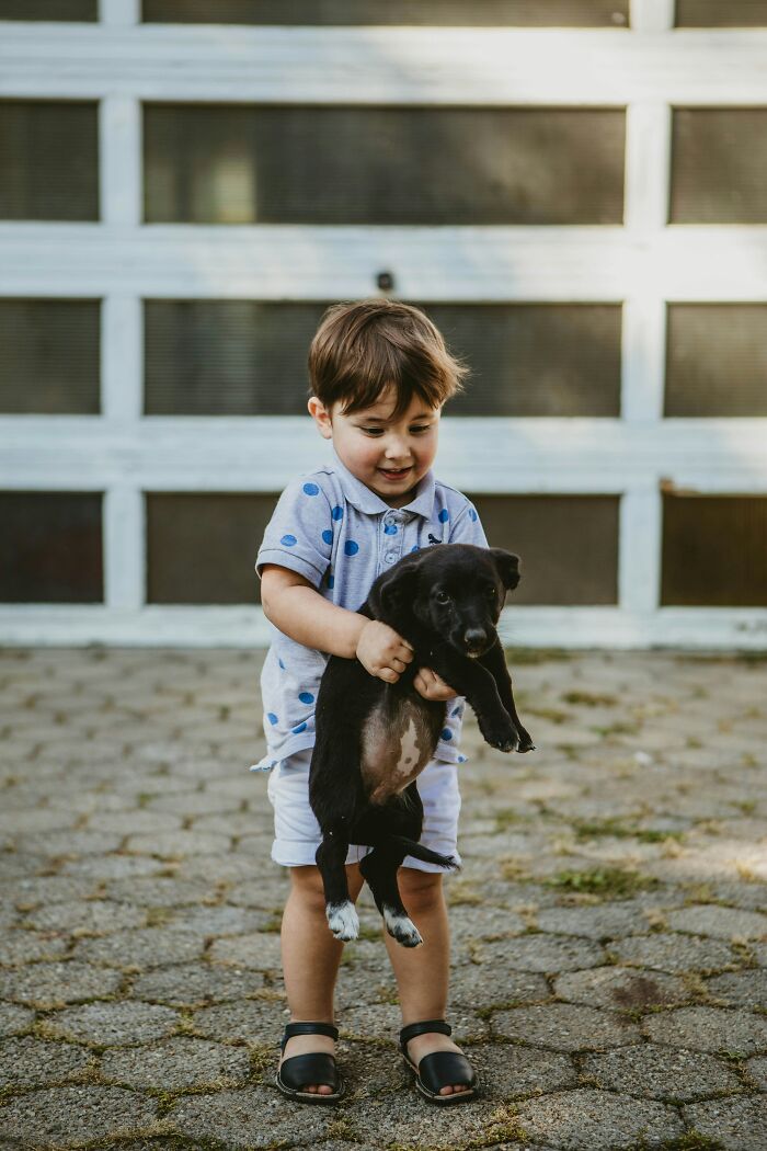 A young boy happily holding a black puppy, a human habit that might confuse dogs.