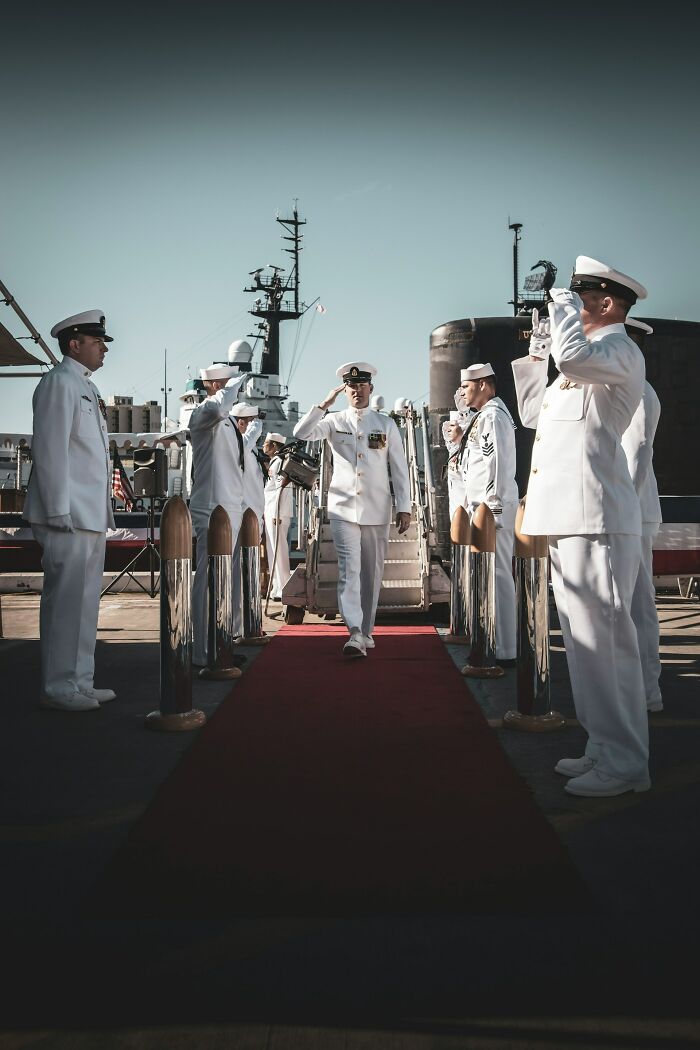 Military personnel in white uniforms saluting on a red carpet, suggesting a public persona versus private double lives.