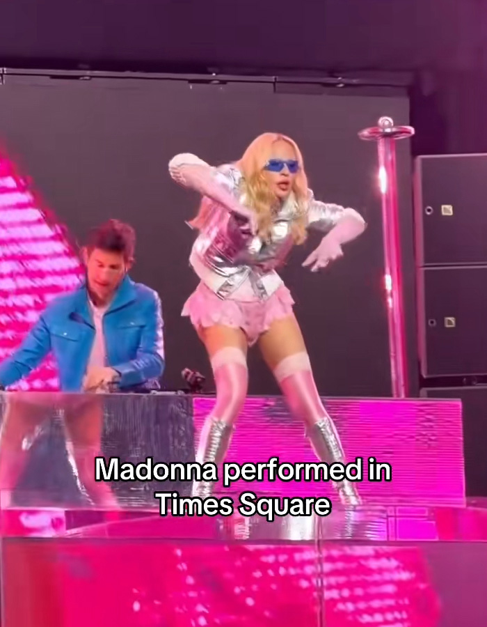 Madonna performing in Times Square, wearing a silver jacket and pink outfit, sparking hilarious reactions.
