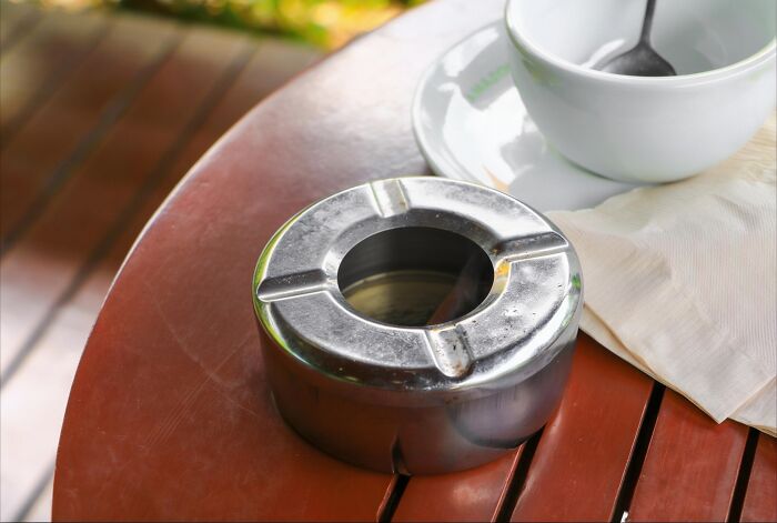 Metal ashtray on wooden table with cup and napkin family secrets