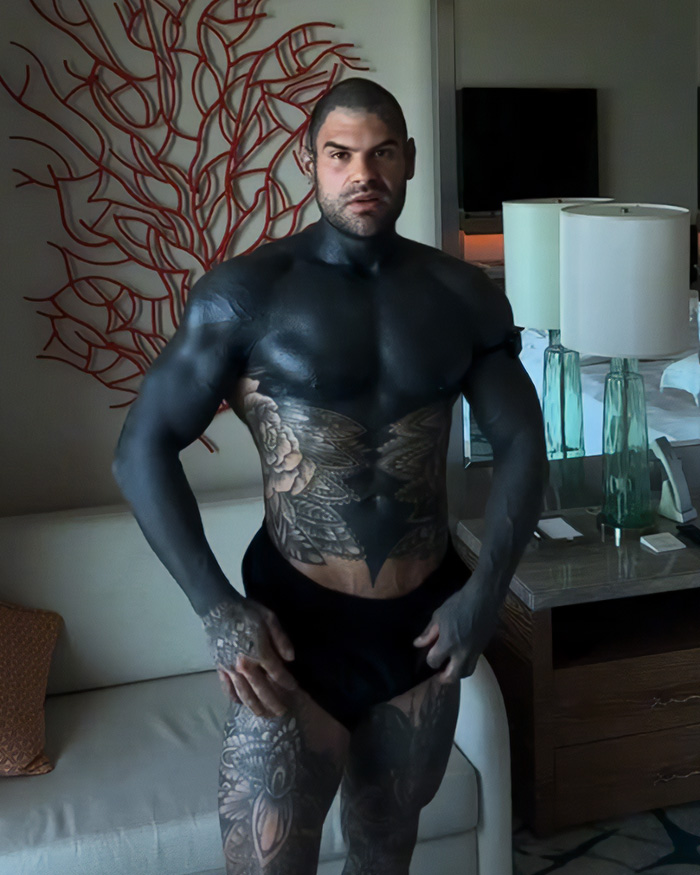 A man with extensive blackout tattoos and some intricate designs on his torso and legs, showcasing the blackout tattoos trend.