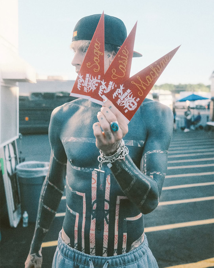 Man with blackout tattoos wearing a backward hat and holding pennants, showing his extensive ink trend.