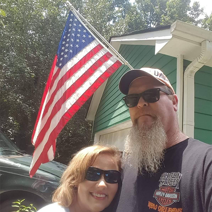 Man loses his temper, posing with his wife outdoors under an American flag.