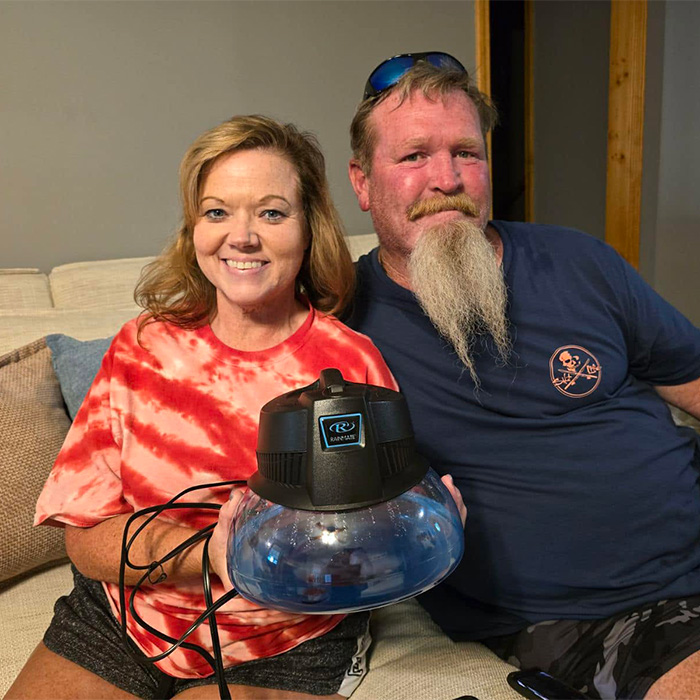 Man loses his temper, sitting with his wife who holds a humidifier, both smiling on a couch.