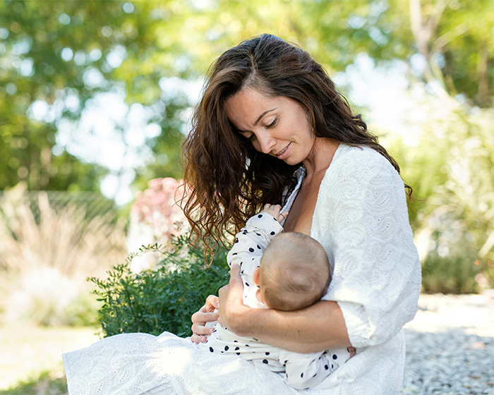 Mother breastfeeding baby outdoors in garden setting Mother breastfeeding baby outdoors in garden setting