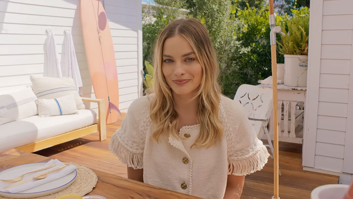 Margot Robbie smiles brightly, a famous Potterhead, at an outdoor table in a casual setting. Margot Robbie smiles brightly, a famous Potterhead, at an outdoor table in a casual setting.