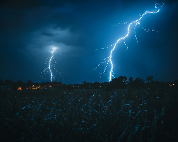 Two bolts of lightning striking a dark field at night, highlighting weirdly hard to forget facts about weather.
