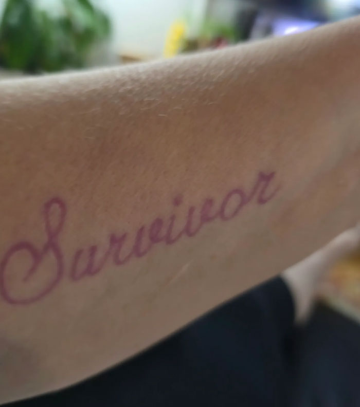 A forearm displaying the word Survivor in elegant script, highlighting meaningful tattoos.