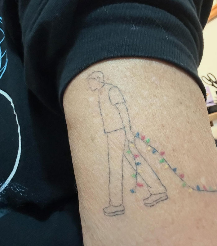 An arm tattoo of a man dragging colorful Christmas lights, an example of meaningful tattoos.
