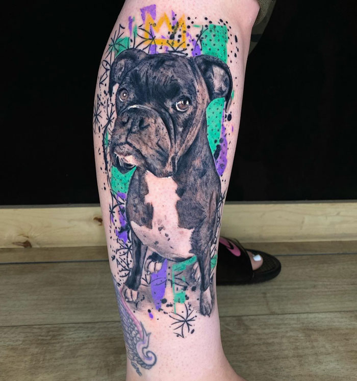 Vibrant boxer dog portrait tattoo on leg with green and purple abstract background, showing meaningful tattoos.