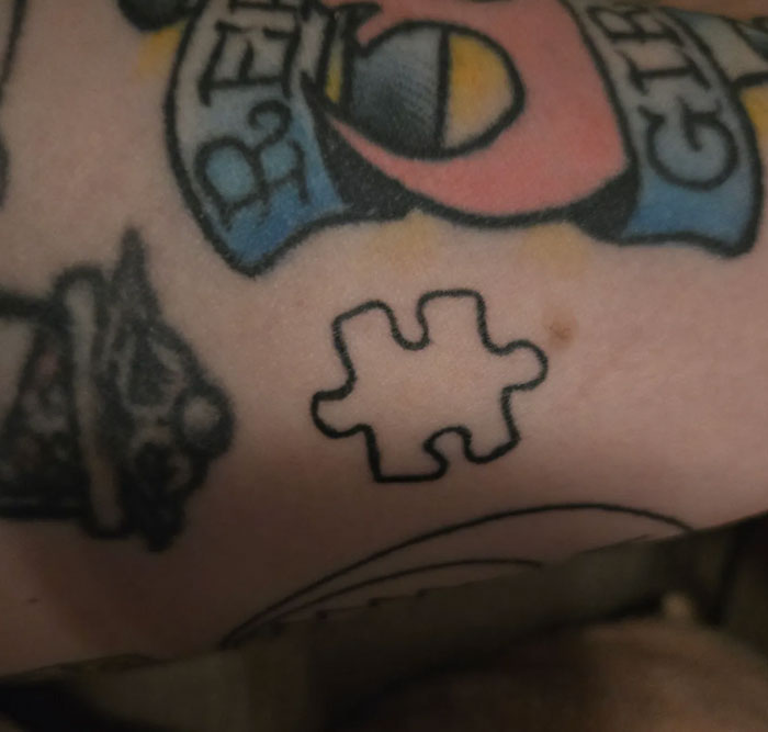 A close-up of an arm with several tattoos, including a prominent outline of a puzzle piece. This tattoo holds a special meaning.