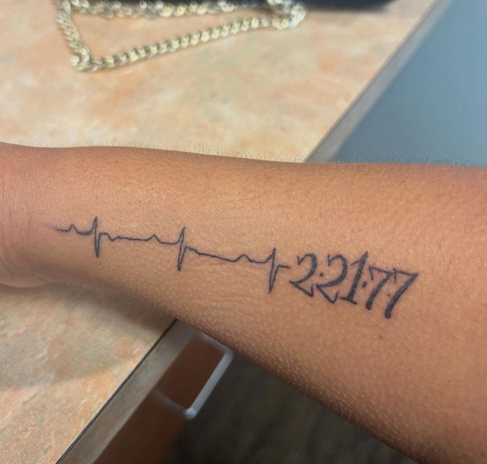 A heartbeat line tattoo on an arm, with the date 2:21:77 marking a significant moment.