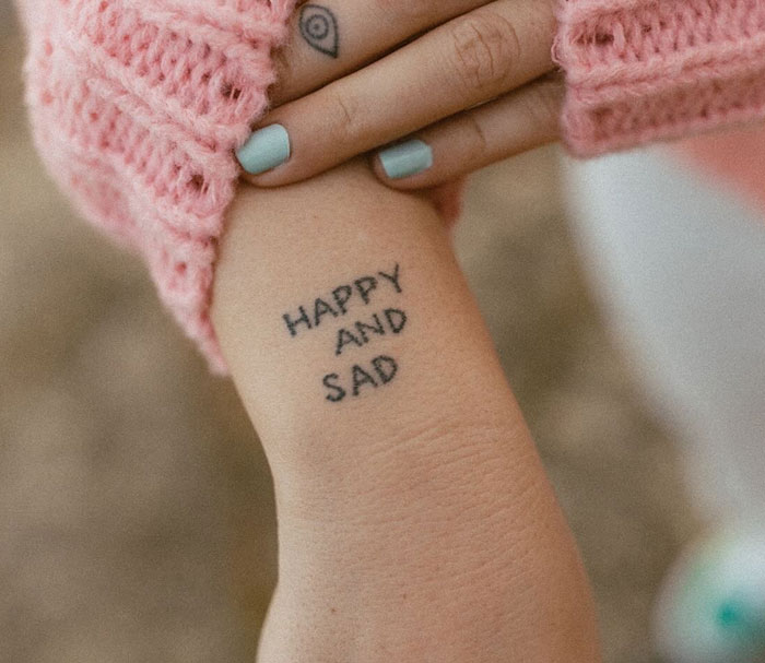 Close-up of a person's wrist with the words HAPPY AND SAD tattooed, symbolizing tattoos that mean far more than what meets the eye. This tattoo expresses complex emotions.