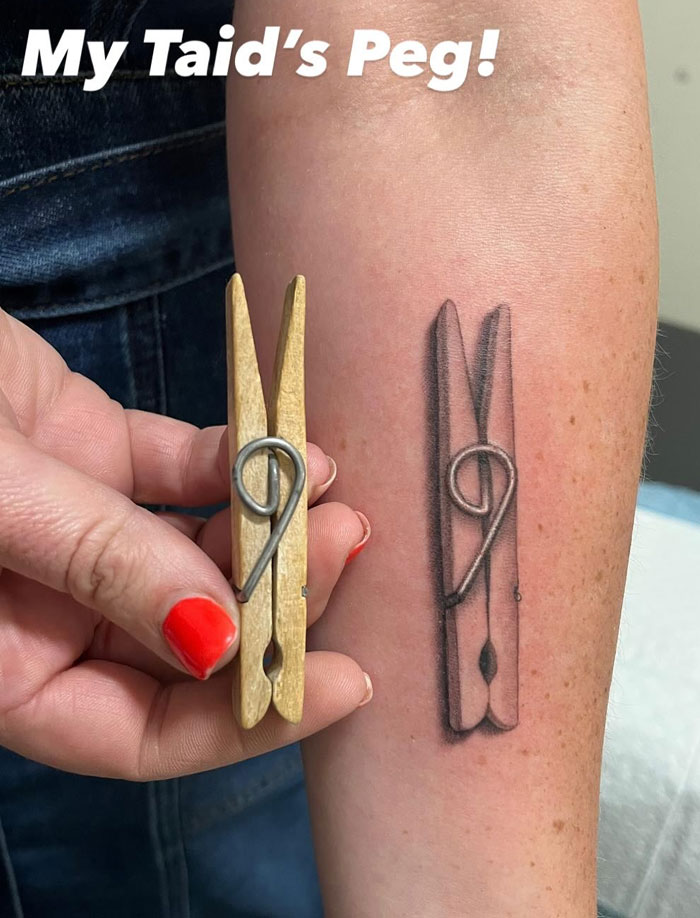 A realistic tattoo of a wooden clothespin next to an actual clothespin held by a hand, showing a meaningful connection.