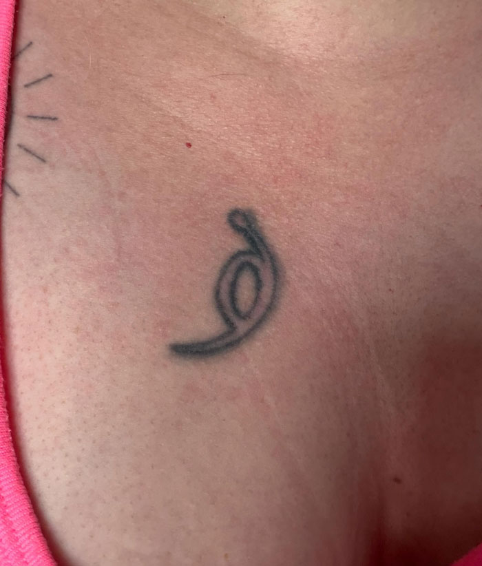 A small, abstract symbol tattoo on a person's collarbone. This unique tattoo has a deeper meaning.
