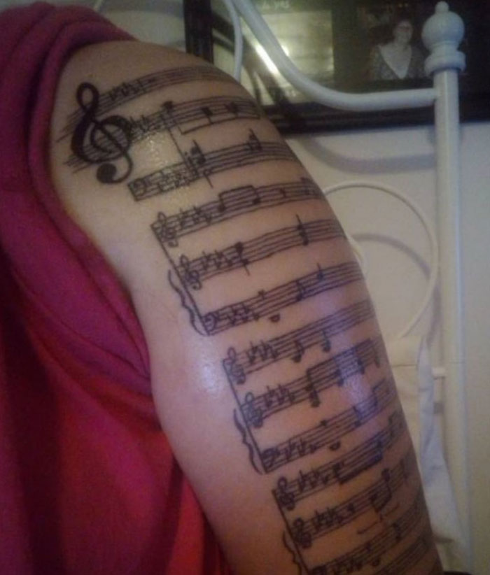 An arm covered in a detailed musical staff tattoo with notes and a treble clef, showcasing meaningful tattoos.