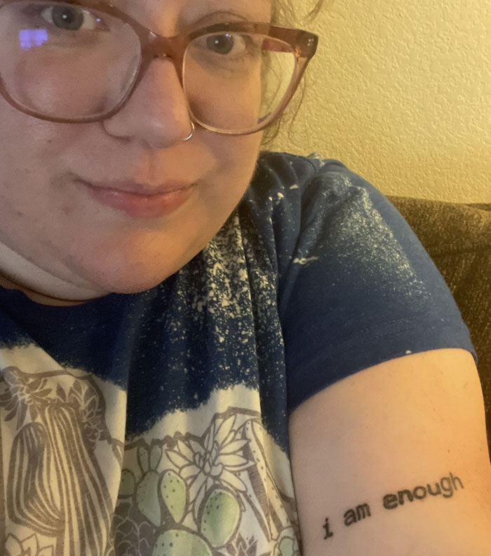 A woman proudly displays her arm tattoo that reads I am enough, a meaningful expression of self-worth.