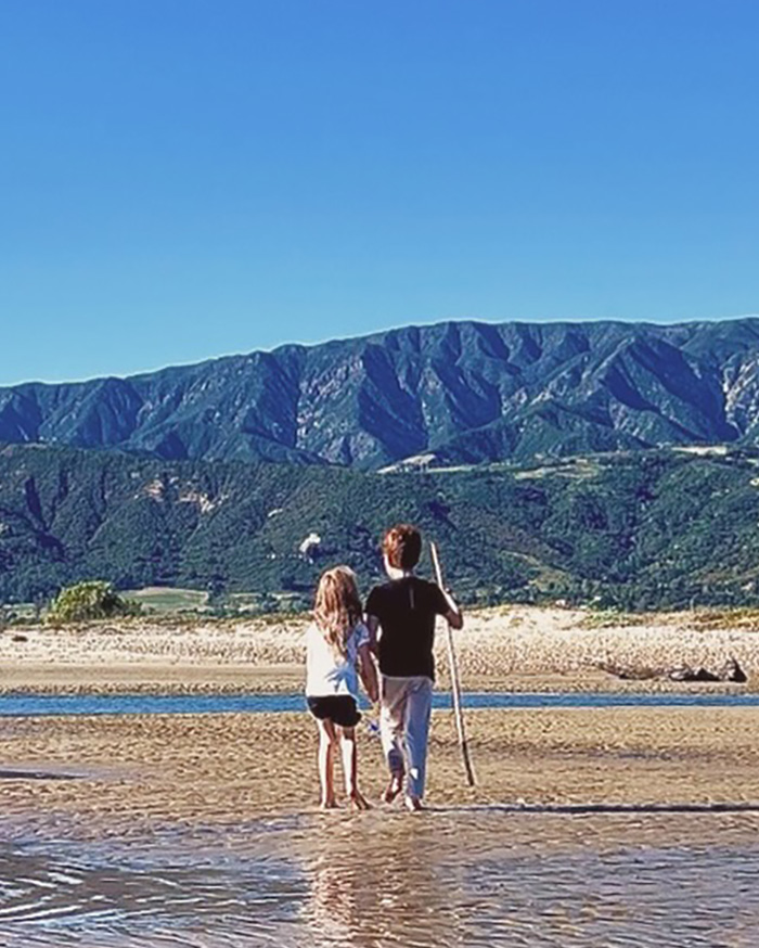 Children walking barefoot on beach with mountains in background