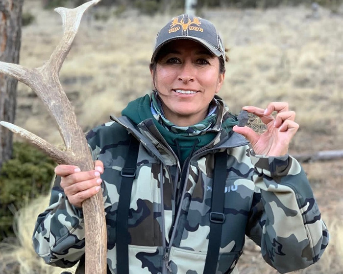Woman holding deer antler and small object wearing hunting gear outdoors Woman holding deer antler and small object wearing hunting gear outdoors