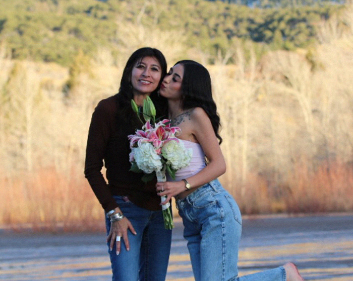 Woman holding flowers with young woman kissing her cheek outdoors Woman holding flowers with young woman kissing her cheek outdoors